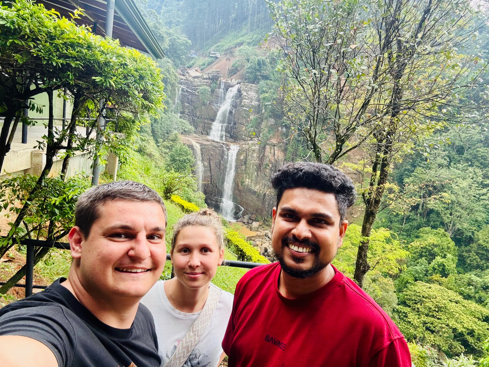 A guide and two guests taking a selfie with a beautiful waterfall in the Sri Lankan hills behind them